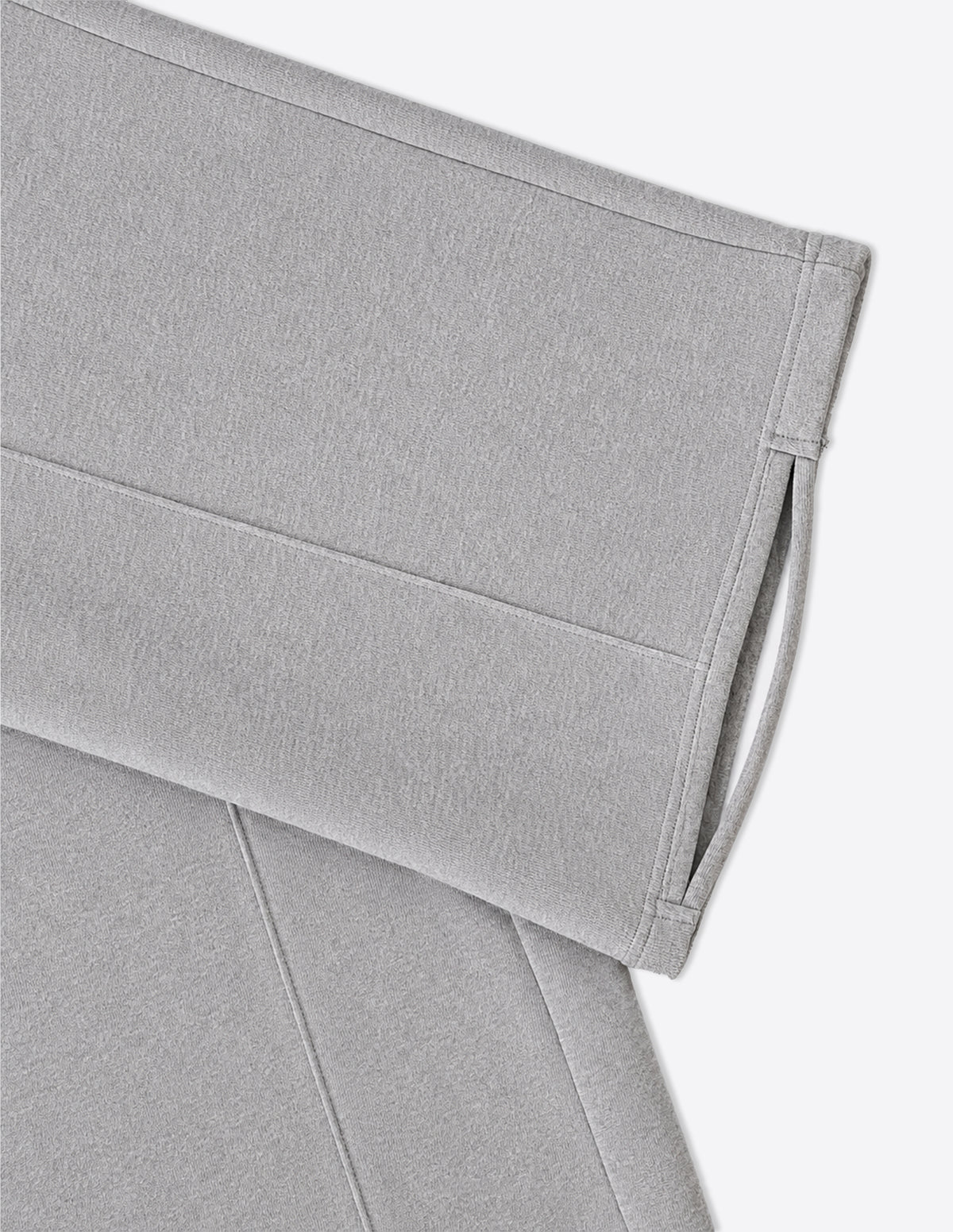 Detalle del bajo del pantalón gris con tira pasante de tejido para el pie, mostrando el diseño funcional del bajo oversize.