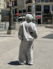 Sudadera oversize unisex gris de WAENN con detalle del logo en la espalda, presentada en un estilismo urbano en la calle.